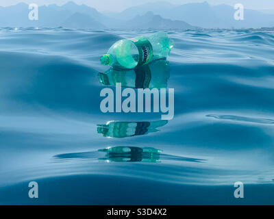 Floating green crown empty plastic bottle with glossy reflections in waves - award winning photo
