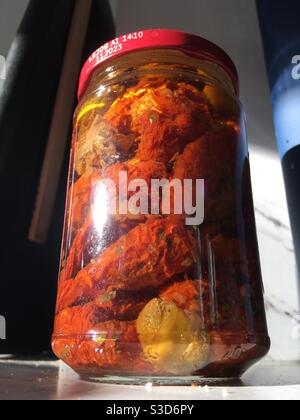 A jar of sun dried tomatoes on a kitchen counter, drenched in sunlight
