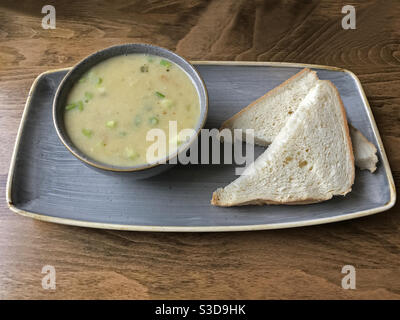 An artisan vegetable soup, featuring sweet potato, leek, apple, and celery is shown alongside two slices of white bread, plated on a table in a cafe. Stock Photo