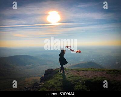 Woman standing on the edge of a cliff holding a scarf blowing in the wind Stock Photo