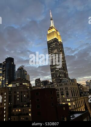 Silhouette of the Empire State building with golden white lights against the twilight sky with puffy gray clouds before a storm, New York City, USA Stock Photo