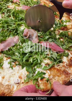 Man cutting a gourmet pizza with a metal pizza wheel, USA Stock Photo