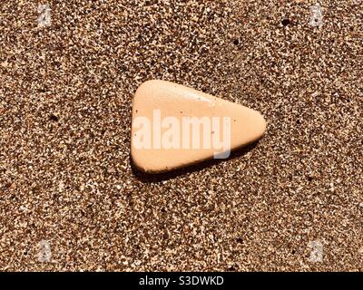 A rock that looks like a play button icon placed on sandy beach Stock Photo