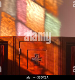Stained glass filtered light in a Catholic Church shines on a confessional booth Stock Photo