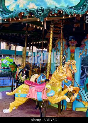 A beautiful golden carousel cat and horse followed by a green frog on the ornate colorful merry-go-round At Bryant Park, Manhattan, New York City, USA Stock Photo