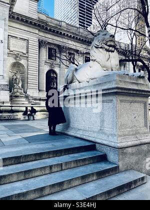 A woman pets the tail of the lion statue In front of the New York public library Stock Photo