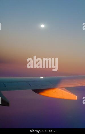 Moonrise over the Pacific, above the glow of sunset, approaching the island of Maui, Hawaii, USA. Full moon reflected on the wing, photographed from a window seat. 10000 meters. Stock Photo