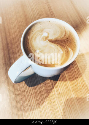 Latte or cappuccino coffee in a white mug on a wooden table. Stock Photo