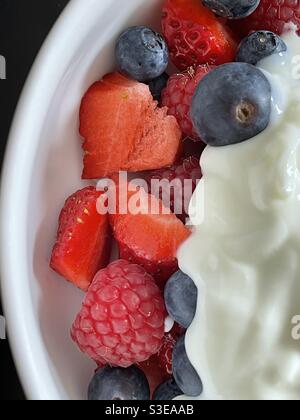 Fresh blueberries, strawberries and raspberries with plain yoghurt in a white china bowl Stock Photo