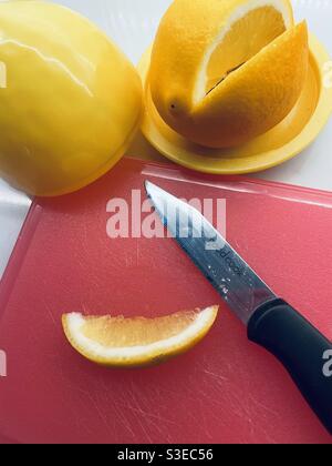Close up of a sliced Meyer lemon on an orange cutting board with a very sharp paring knife Stock Photo