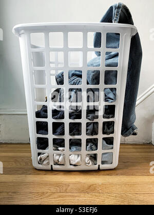 Laundry in white plastic basket near laundry room, a pair of jeans hanging over side Stock Photo