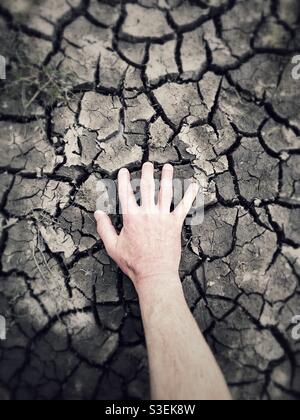 A human hand reaching for water in a dried and cracked river bed Stock Photo