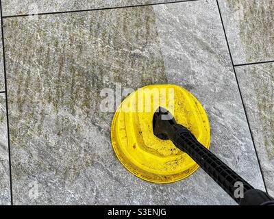 Attachment on a pressure washer being used to clean porcelain paving slabs on a garden patio, with contrast between clean and dirty areas Stock Photo