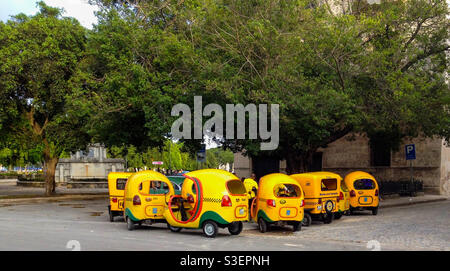 Group of quaint yellow Coco taxis parked waiting for customers in Havana, Cuba Stock Photo