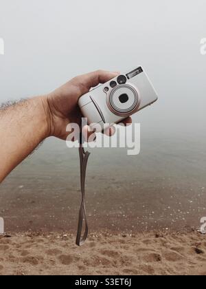 Man holding a point and shoot camera against misty sea view Stock Photo