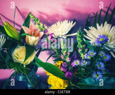 A photograph of beautiful bouquets of flowers in glass vases against a pink painted wall Stock Photo