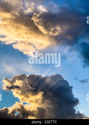 Rays of sun light beaming sunbeams through the fluffy white and grey clouds, blue sky Stock Photo