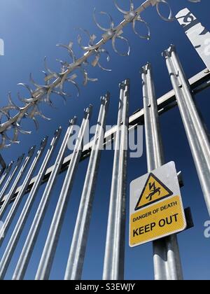 A warning sign stating danger of death to trespassers on a metal fence with barbed wire Stock Photo