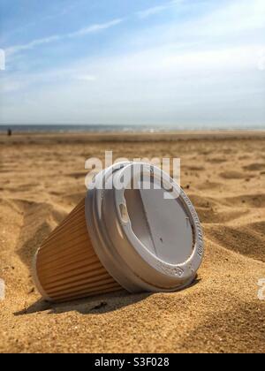 A single use takeaway non-recyclable cardboard and plastic coffee cup washed up on a sandy beach in an environmental issues concept Stock Photo