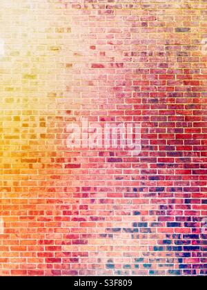A full frame background of a colourful and brightly lit red brick wall with yellow and red hues with copy space Stock Photo