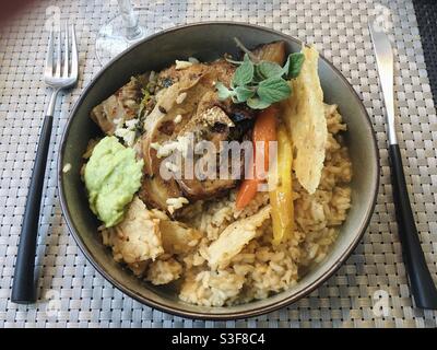 Pork chop meat and steamed vegetables over rice in a restaurant plate dish on a weaved table mat with fork and knife Stock Photo