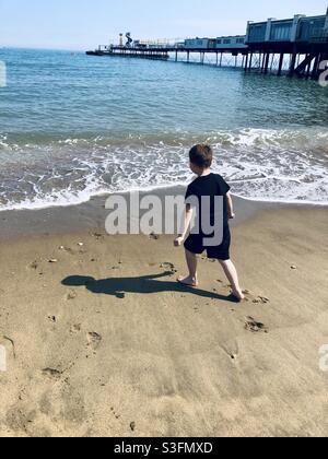 Boy playing on beach with pier in background Stock Photo