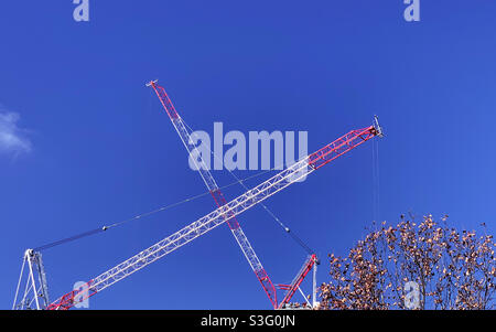 X marks the spot. Two large red and white cranes crossed over to form a letter x in the blue sky Stock Photo