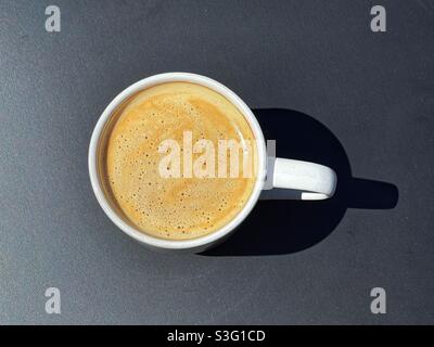 Overhead closeup view of a cup of fresh coffee in a white cup on a black tabletop Stock Photo