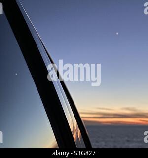 Sunset over the Pacific Ocean reflected in windows of a parked car, California, USA. Soft focus white object in sky is great conjunction between Jupiter and Saturn Stock Photo