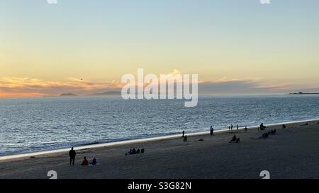 Silhouetted people on beach at Point Mugu, California, with sun setting over the Pacific Ocean. Catalina Island visible on the horizon Stock Photo
