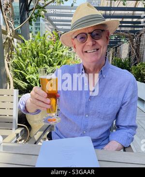 Handsome and happy senior man enjoying a beer at an outside rooftop terrace in Midtown Manhattan on a Summer Day, NYC, USA Stock Photo