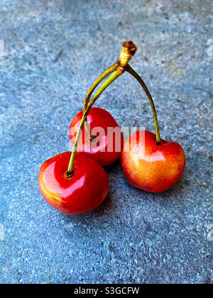 Three fresh cherries with stems on a stone surface. Stock Photo