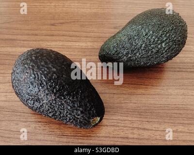 Two avocados on brown wood surface Stock Photo
