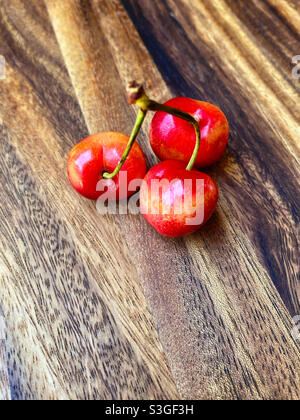 Three ripe cherries on a wooden board Stock Photo