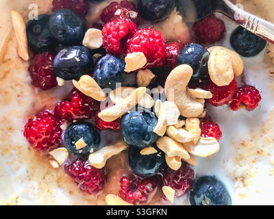 Close up view of porridge with raspberries, blueberries and cashew nuts for breakfast. Stock Photo