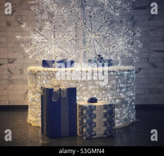 Presents wrapped in blue wrapping paper, at the base of a lit-up white artificial Christmas tree. Stock Photo