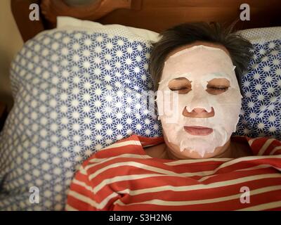 Women wearing a beauty facemask resting on a bed Stock Photo