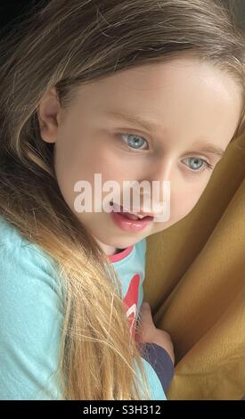 Beautiful blue eyed  little girl with long hair looking through window Stock Photo