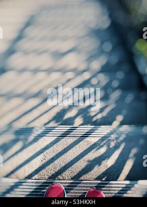 Pink tips of sneakers heading down shadowed cement stairs Stock Photo