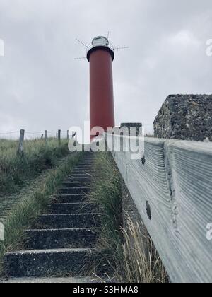 a staircase with a wooden handrail leads to a red lighthouse on a grassy hill at Julianadorp, Netherlands Stock Photo