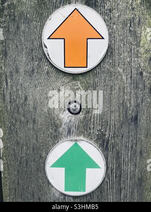 an orange and a green arrow are arranged one above the other on a washed-out gray wooden pole and both point upwards Stock Photo