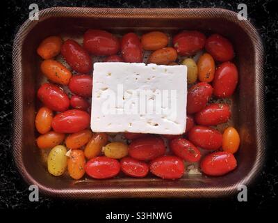 Feta cheese, cherry tomatoes, garlic, herbs, and extra virgin olive oil in a roasting tin Stock Photo