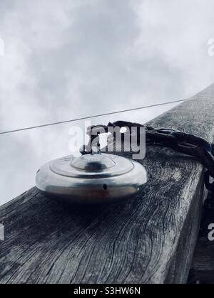 a round padlock hangs on a wooden beam around which a metal chain is wrapped Stock Photo