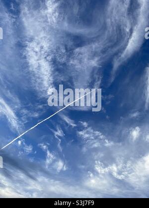 Deep blue skies with white fluffy clouds and airplane contrail Stock Photo