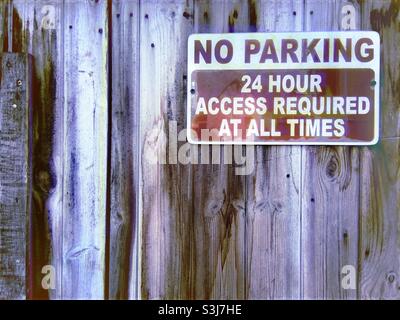 No Parking sign on a wooden panelled door. The metal sign says ‘No Parking. 24 Hour Access Required At All Times’. Stock Photo