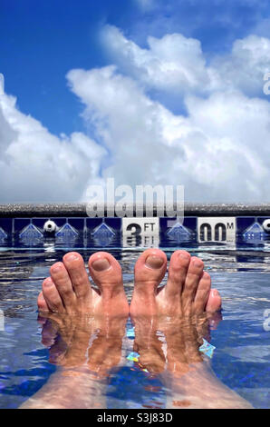 Two feet sticking out of the water at the 3 foot end of an outdoor swimming pool Stock Photo