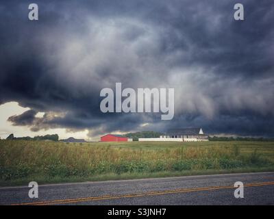 Incoming storm clouds over farm house and field Stock Photo