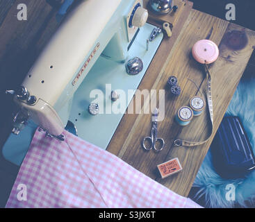 Vintage, Harris sewing machine in powder blue and accessories, seen from above on a wooden table. Machine has pink and white checkered fabric under the needle Stock Photo