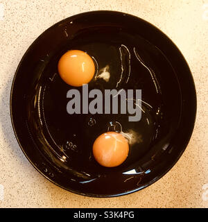 Two eggs broken on black plate with yolk Stock Photo