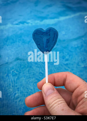 Blue love heart lollipop against a blue swimming pool background.  Heartbroken.  Longing.  Romance Stock Photo